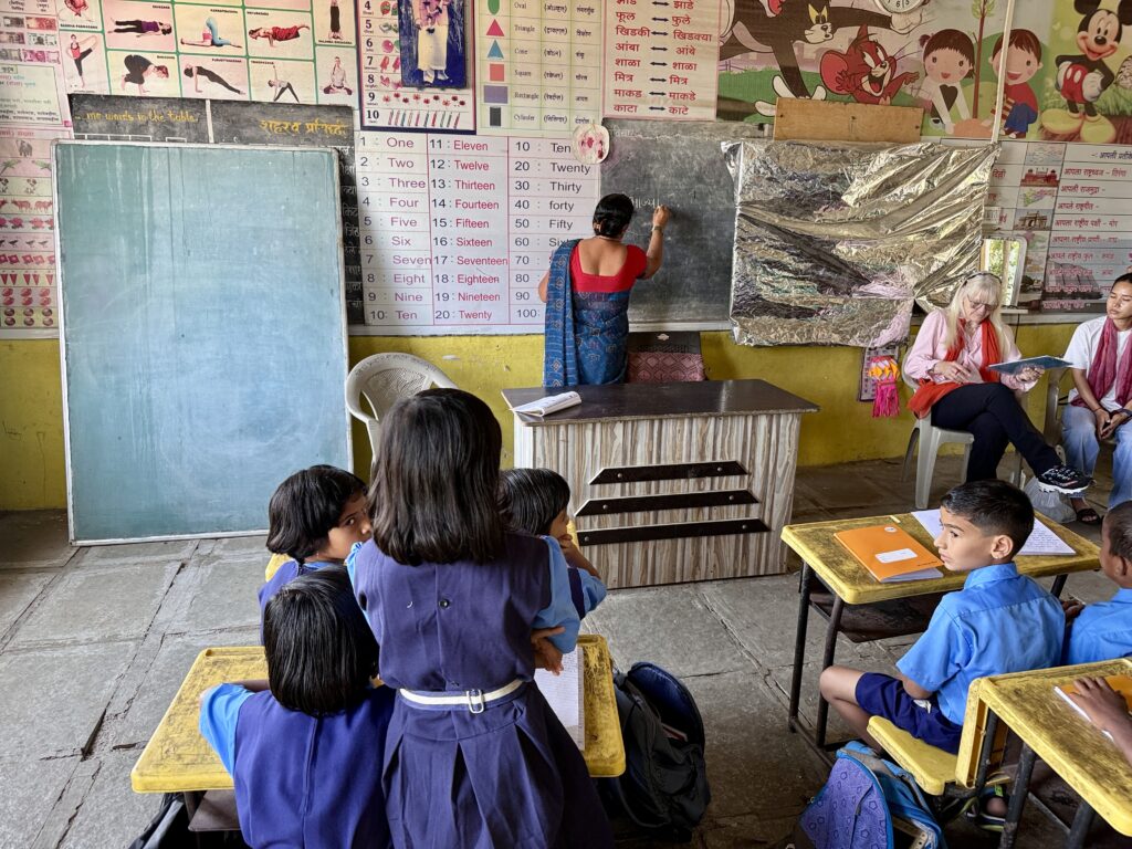 Children and adults in a classroom with a teacher at the chalkboard
